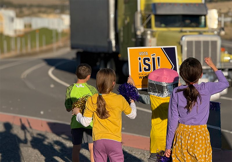 Kids waving a Vota Sí sign at passing traffic along a Wenatchee road